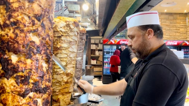 A restaurant worker slices pieces of meat off a spit.