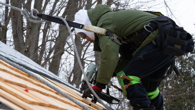 A roofer places shingles on a roof in winter.