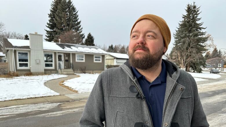 A man stands on a street with solar panels on a home behind him.