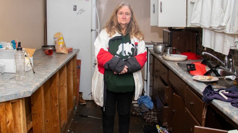 A woman stands in a destroyed kitchen.