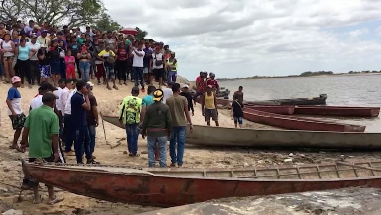 People surround several boats on the shore of a beach. 