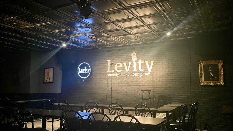 Tables and chairs in a dimly lit room with a spotlighted sign reading 