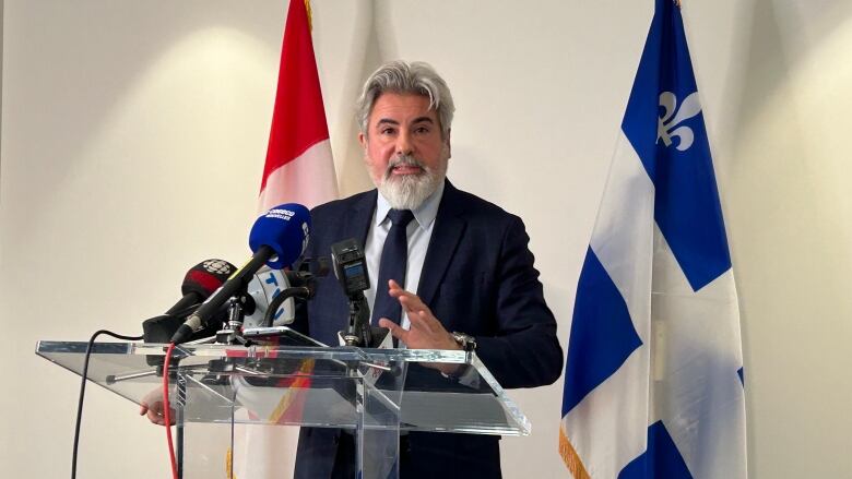 A man stands at a podium in front of flags