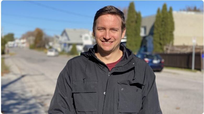 A man stands smiling on the sidewalk 