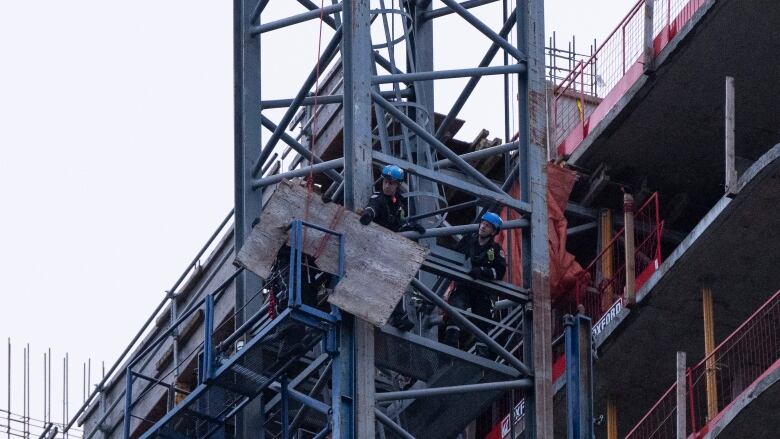 Two workers wearing helmets are beside a high storey of a building. 