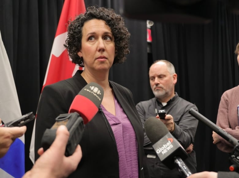 A woman stands in front of microphones.