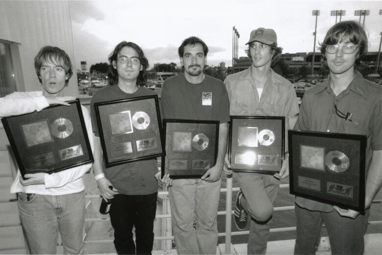 A black-and-white photo shows the band Sloan getting a gold record, along with their manager Chip Sutherland.