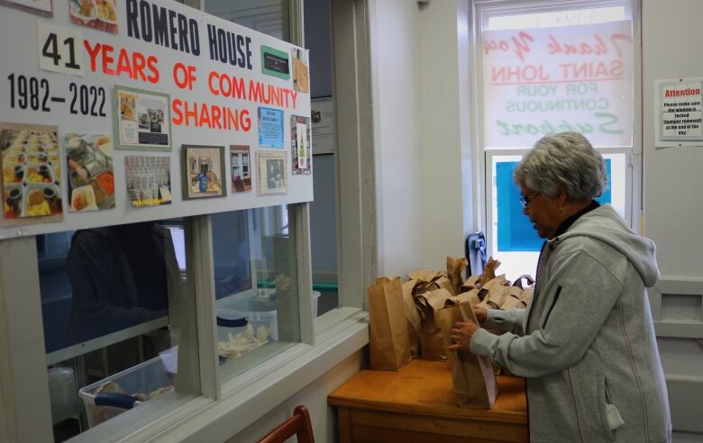 An elderly volunteer picks up bagged lunches at a handmade sign celebrating 41 years at the soup kitchen. 