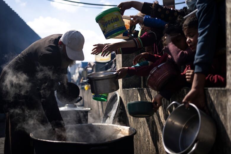 A number of people hold out pots for food.