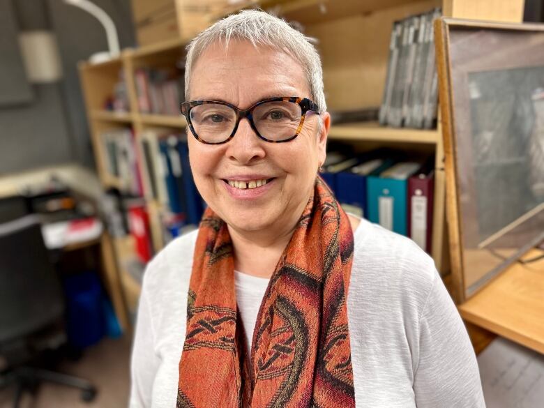 Woman with white hair and glasses smiling in front of a shelf of books