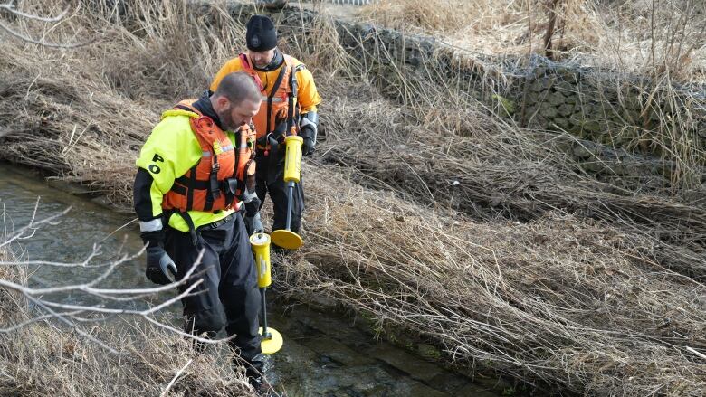 Two cops seen holding detector-type instruments at a waterway.