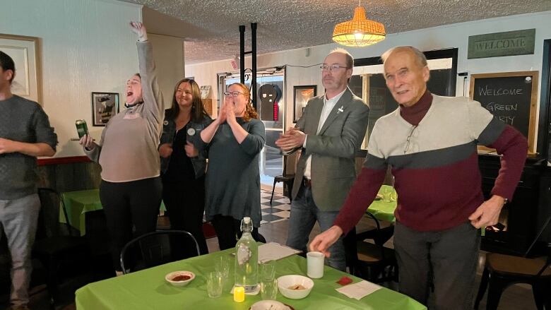 People celebrate while a man in a grey suit looks on -- Matt MacFarlane who won a P.E.I. provincial byelection.