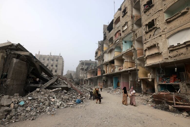 People walk on a road situated between destroyed buildings.