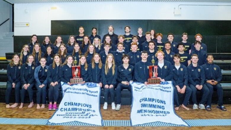 Two swim teams pose for a photo with their banners.