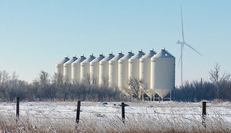 A wind turbine spins behind a row of grain bins.