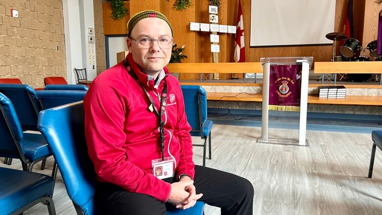 A man sits on a chair in a homeless shelter. 