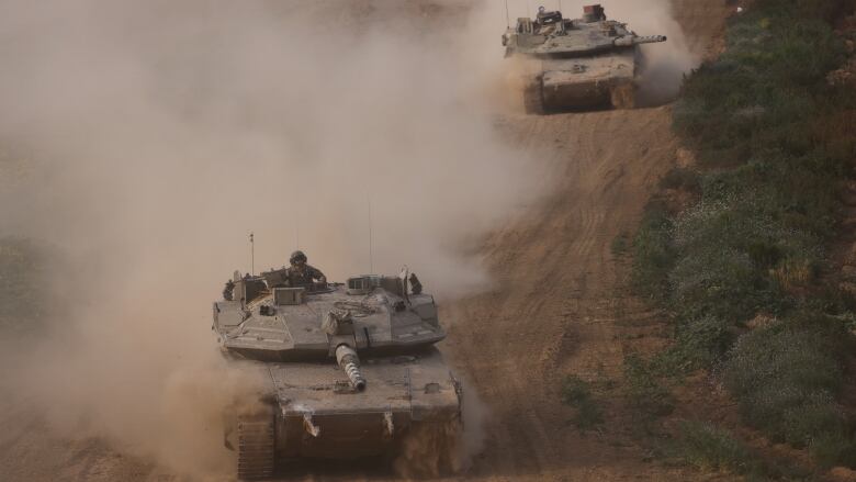 Two military tanks travelling on a dirt road. 