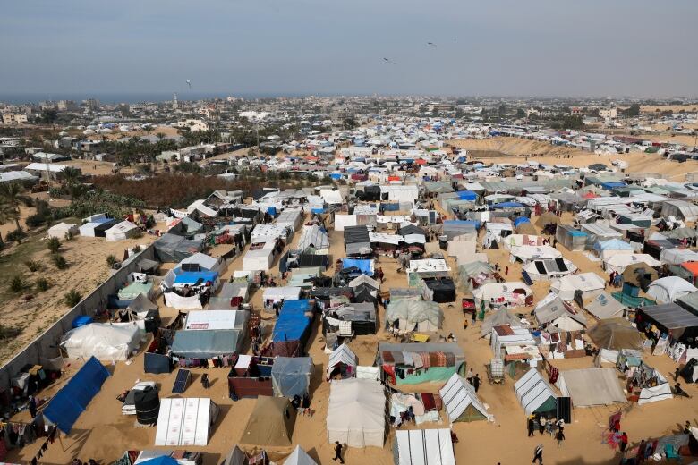 A large encampment of tents and makeshift shelters on a stretch of sand. 