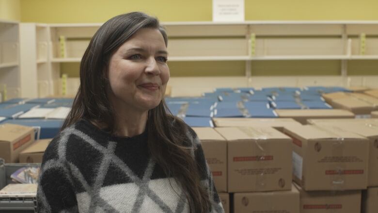 A smiling woman wearing a sweater stands in front of dozens of large cardboard boxes.