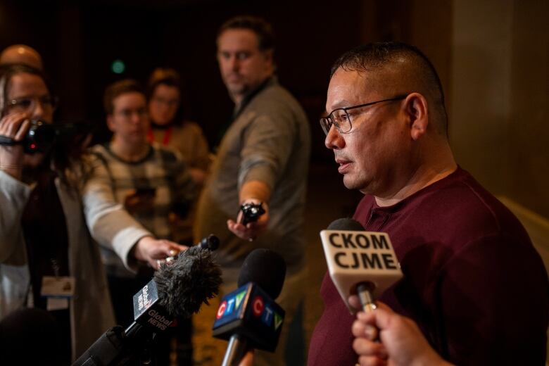 A man in a red shirt speaks into several microphones