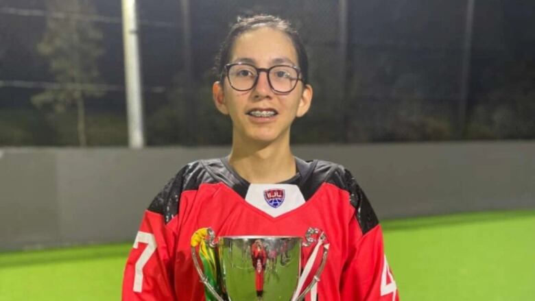 A young boy wearing a lacrosse uniform is holding a champion cup