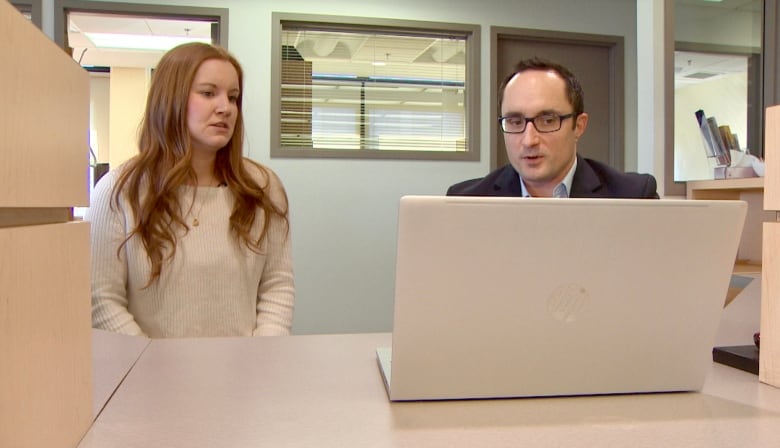 A man and woman sit staring at a computer screen in an office.