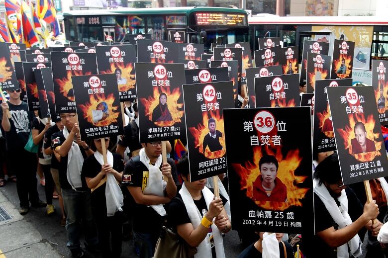 Several people march holding up signs bearing the faces of assorted people.