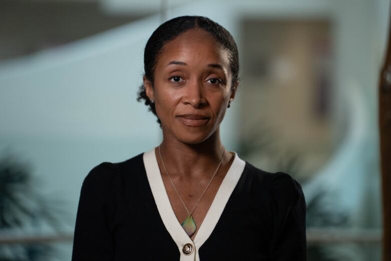 A female physician wearing a black sweater with a white collar and green pendant necklace. 