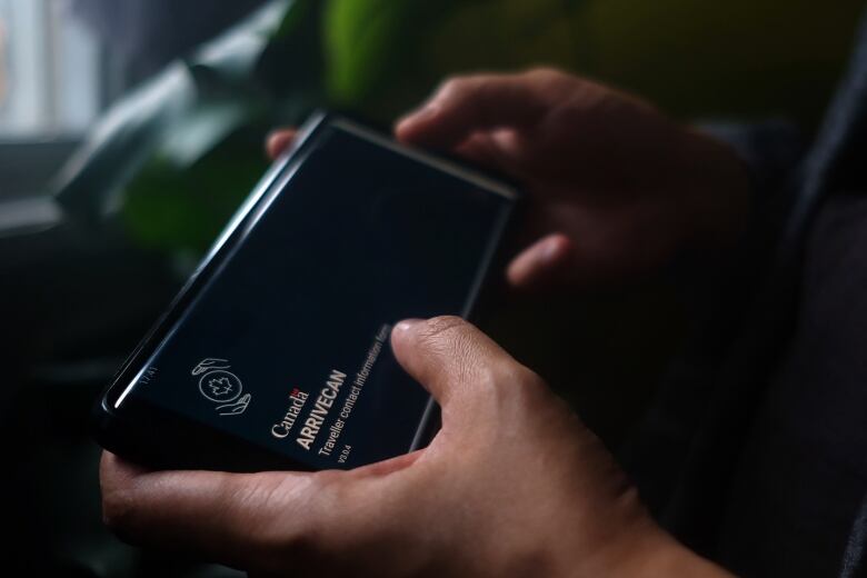 A person holds a smartphone set to the opening screen of the ArriveCan app.