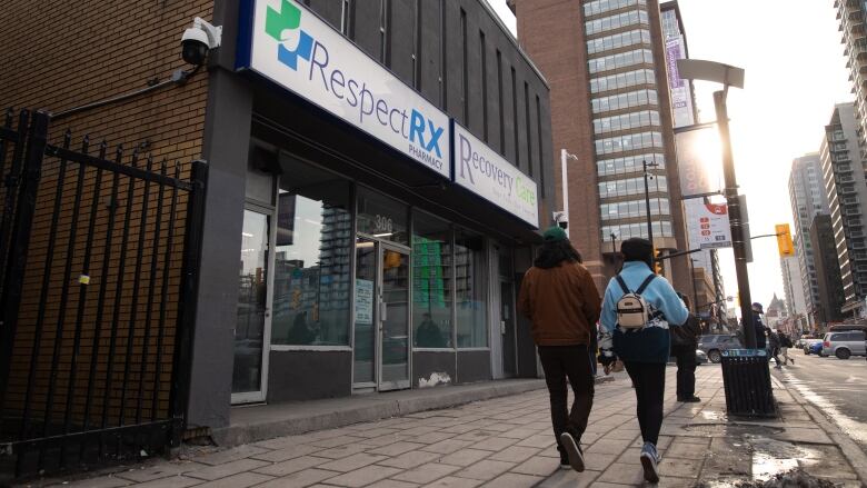 Two people pass a downtown pharmacy.