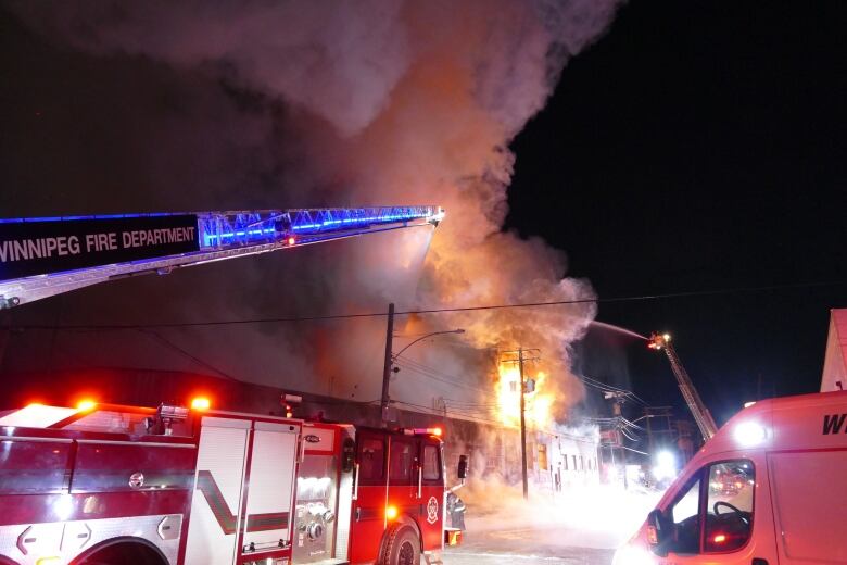 Water is sprayed from a ladder truck onto a burning building below.