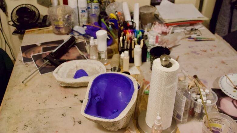 A work bench with a range of tools, art supplies and a model skull on it. 