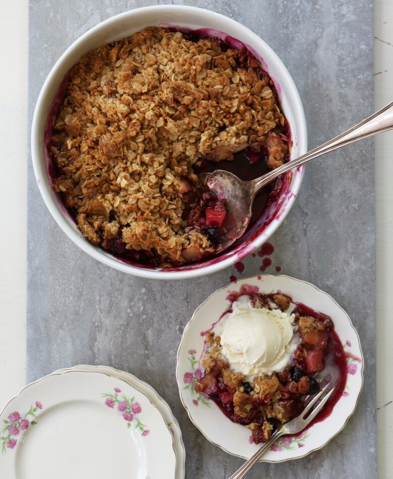 A photo of a big bowl with fruit crumble next to a serving of the dessert with ice cream.