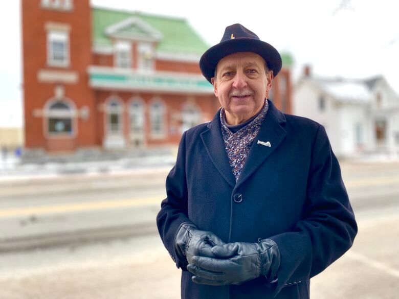 A man smiles at the camera. Wearing a hat and winter coat.