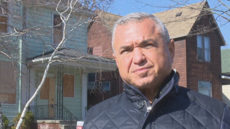 A man stands next to a large house in need of repair.