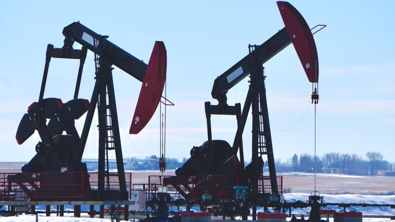 Two black and red oil derricks are pictured in a field with snow.