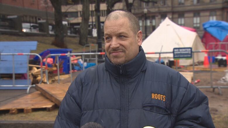 A man stands in front of a tent encampment.