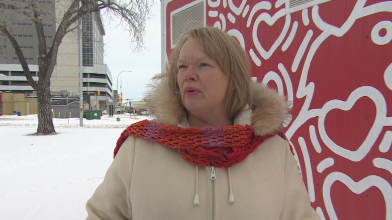 A woman wearing a winter coat is standing in front of a red and white painted structure in winter.