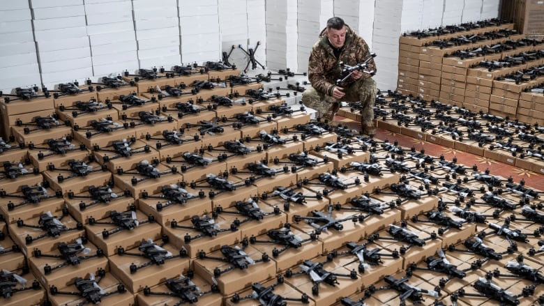 A Ukrainian soldier inspects a drone, surrounded by rows of drones and boxes