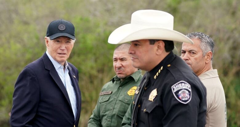 Biden with cap on, surrounded by federal and county authorities. A county sheriff is wearing a white cowboy hat