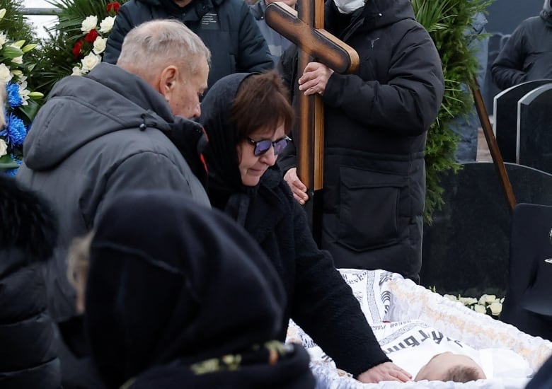 An older man and woman are shown standing above a casket containing a younger man.