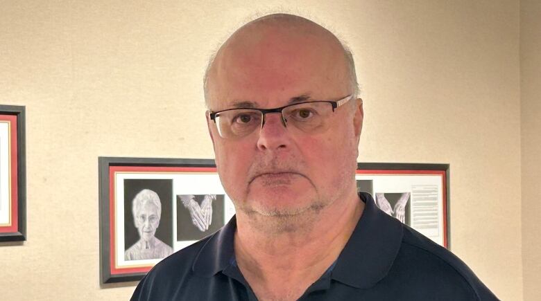 A white man with no hair, wearing glasses and a blue t-shirt.