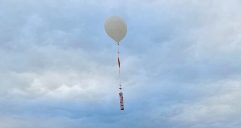 A balloon and long object floating up into the sky.