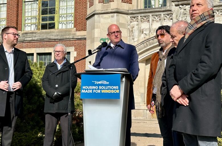 A man speaking at a podium with others around him.