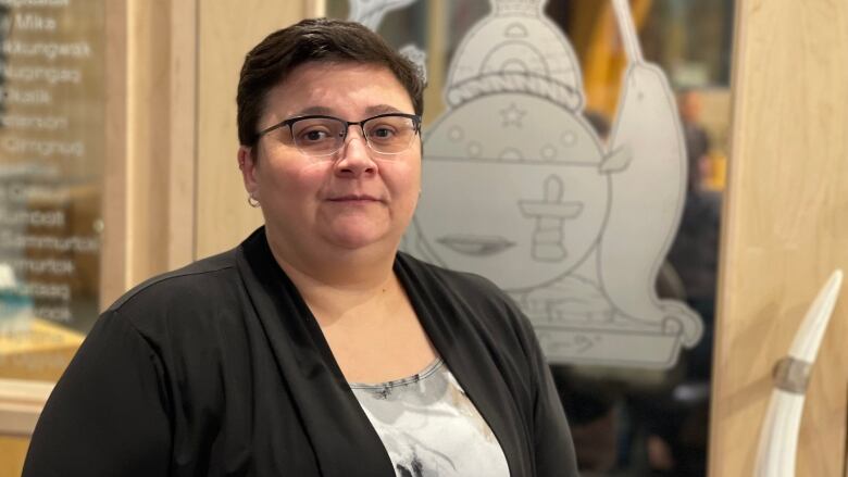 A woman poses in front of a door bearing the coat of arms for Nunavut. 