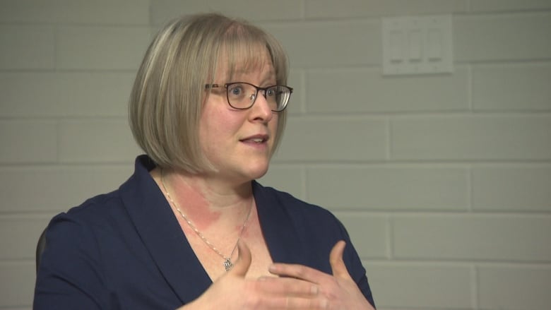 A woman in glasses speaks to someone off-camera.