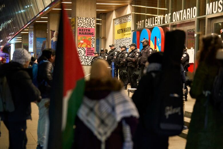 Police stand guard outside a building as protesters gather nearby.