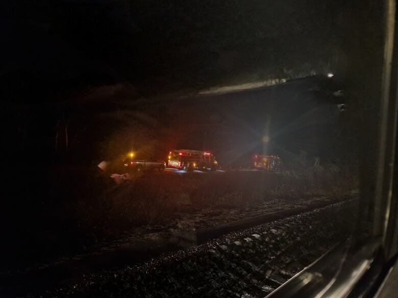 Out a train window there are firetrucks and cars alongside a railway track. 