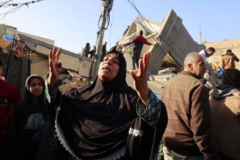 Palestinian woman throws her hands in the air in front of a destroyed building