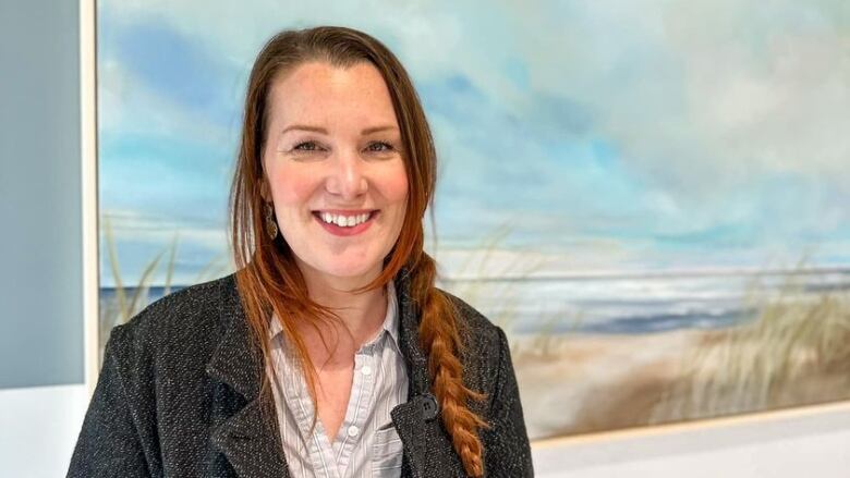 Woman standing in front of painting of beach scene.